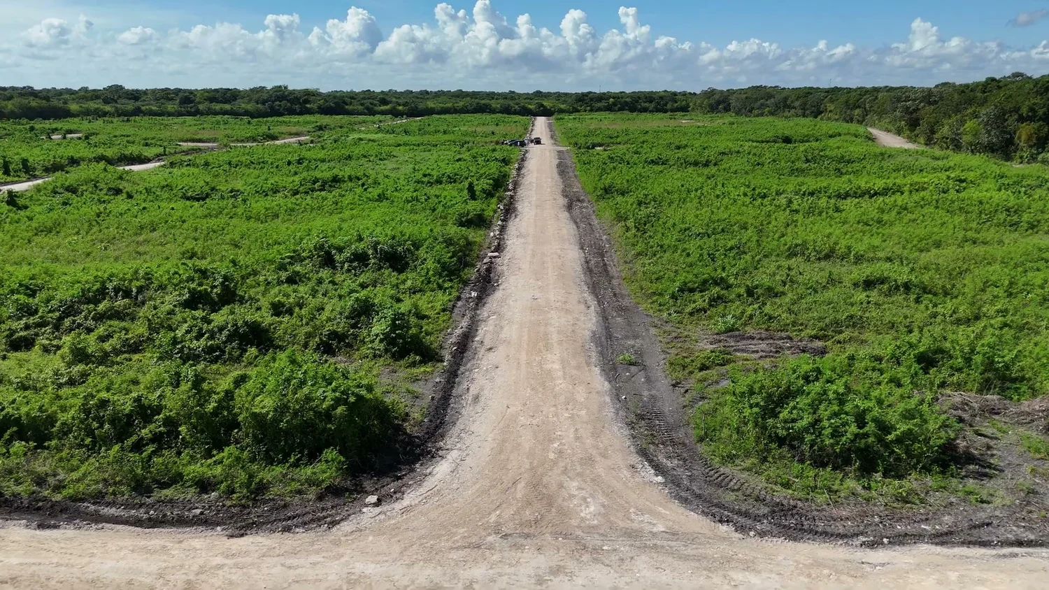 Gravel road running between cleared residential lots under a blue sky in northern Belize