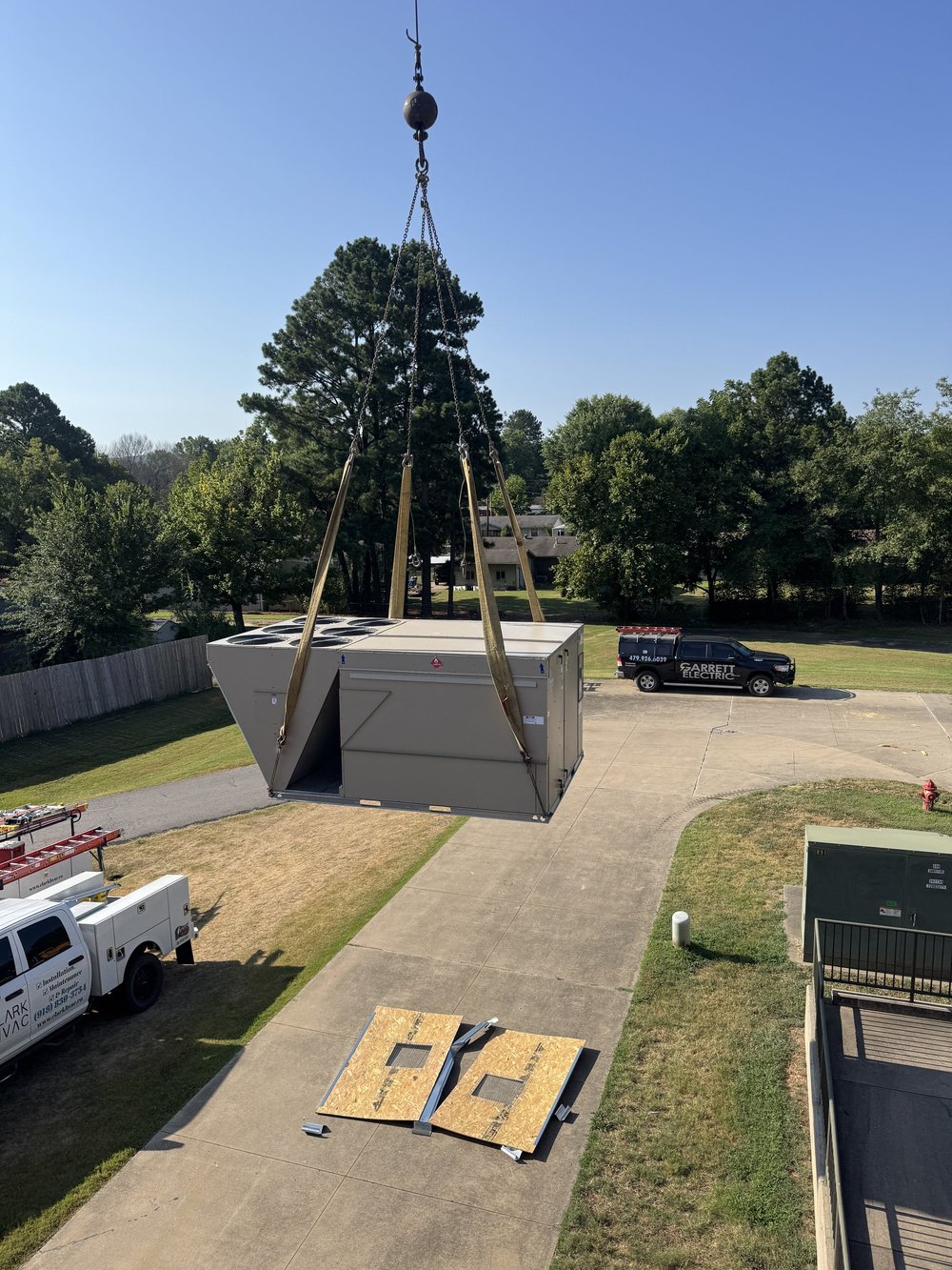 Crane lifting a new commercial rooftop HVAC unit over the lawn at a school in Greenwood, AR, on a Clark HVAC install