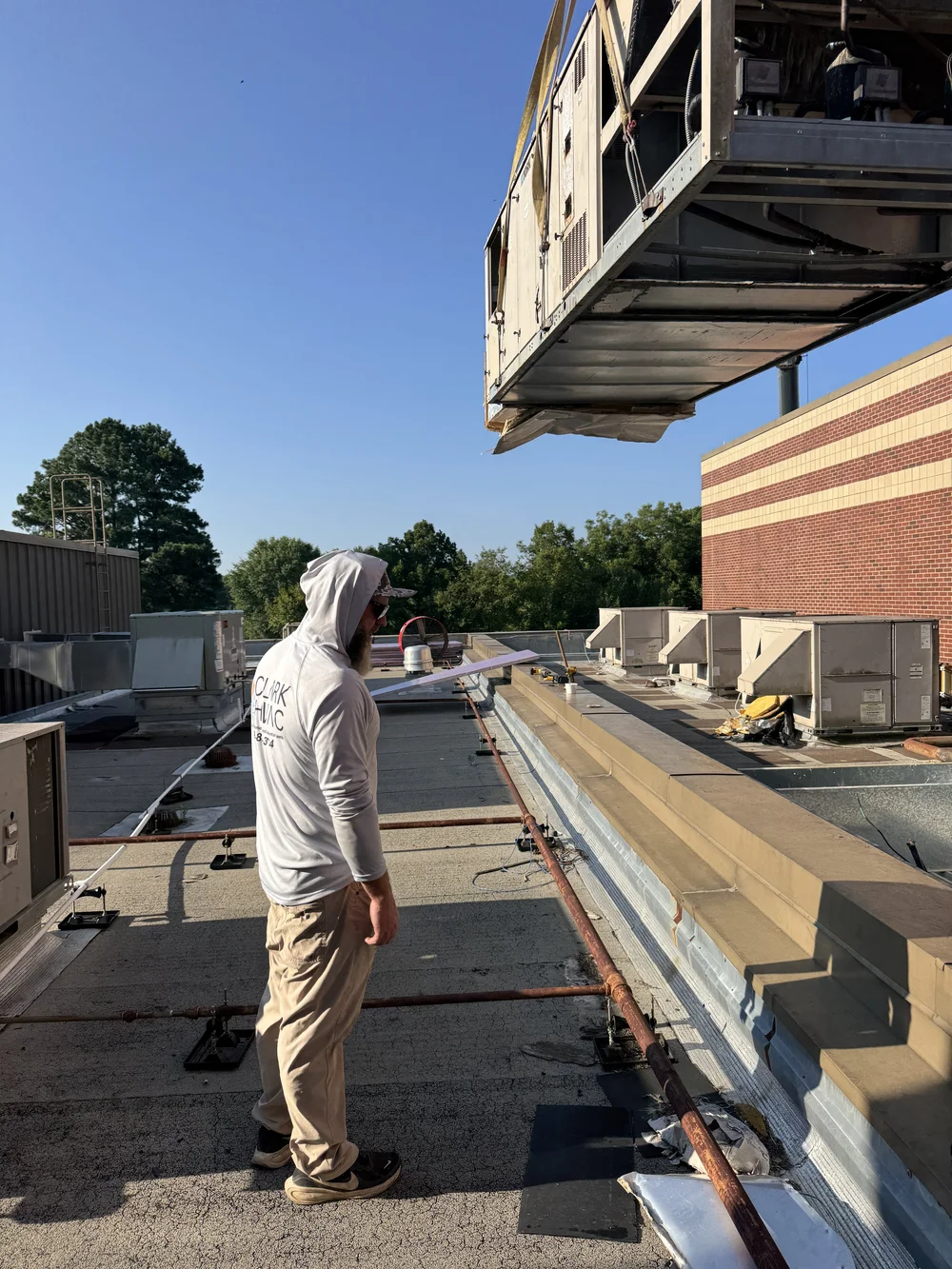 Clark HVAC technician on the roof as a crane sets a commercial rooftop unit at a school in Greenwood, AR