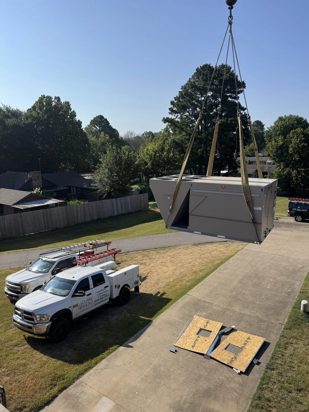 Clark HVAC service trucks below a crane lifting a commercial rooftop unit at a school in Greenwood, AR