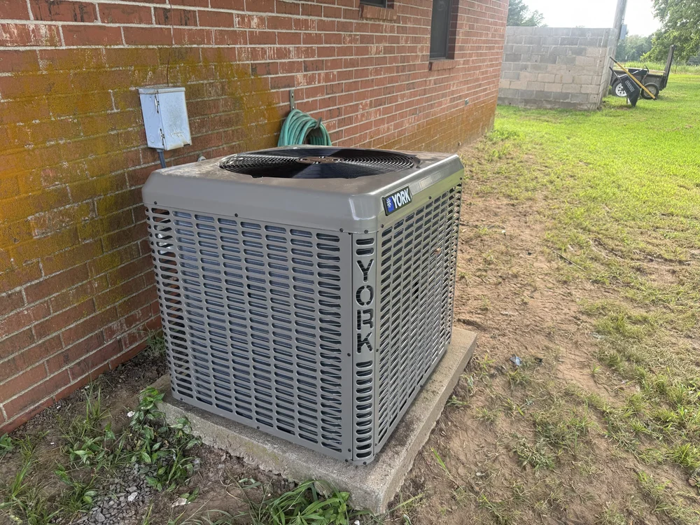 New York AC condenser on a pad beside a brick home near Keota, OK, installed by Clark HVAC
