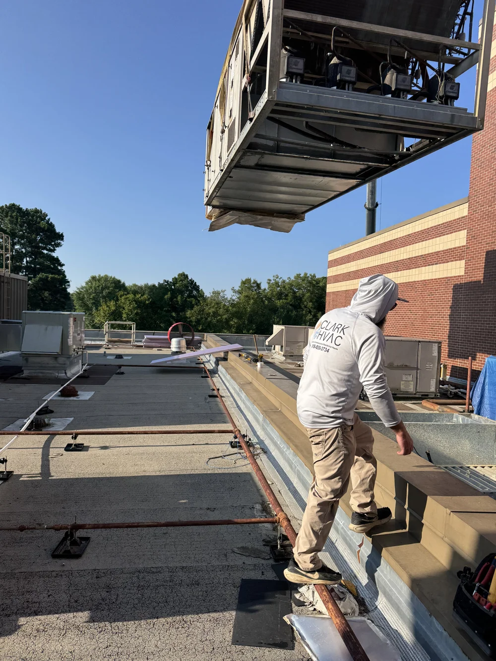 Clark HVAC technician on the roof guiding a crane-set rooftop unit into place at a school in Greenwood, AR