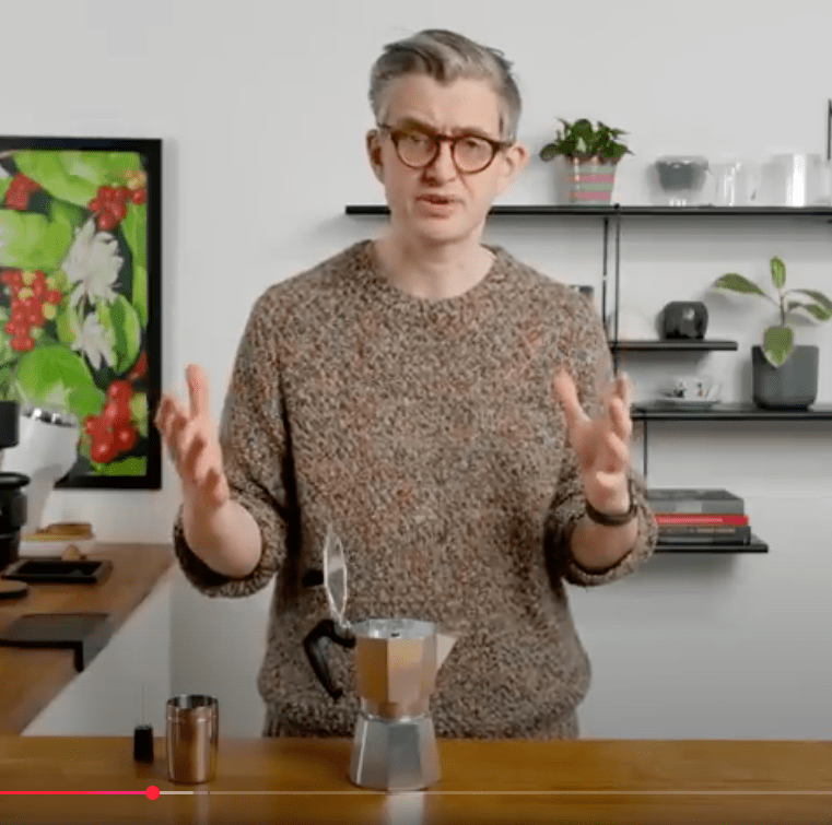 Jamkes Hoffam standing behind a desk talking about coffe in a mocka pot