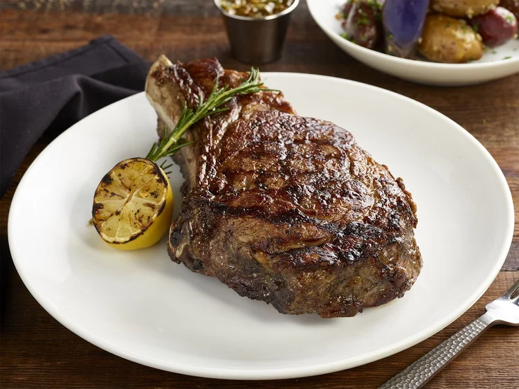 Bone-in ojo de bife ribeye steak with grilled lemon and rosemary on a white plate
