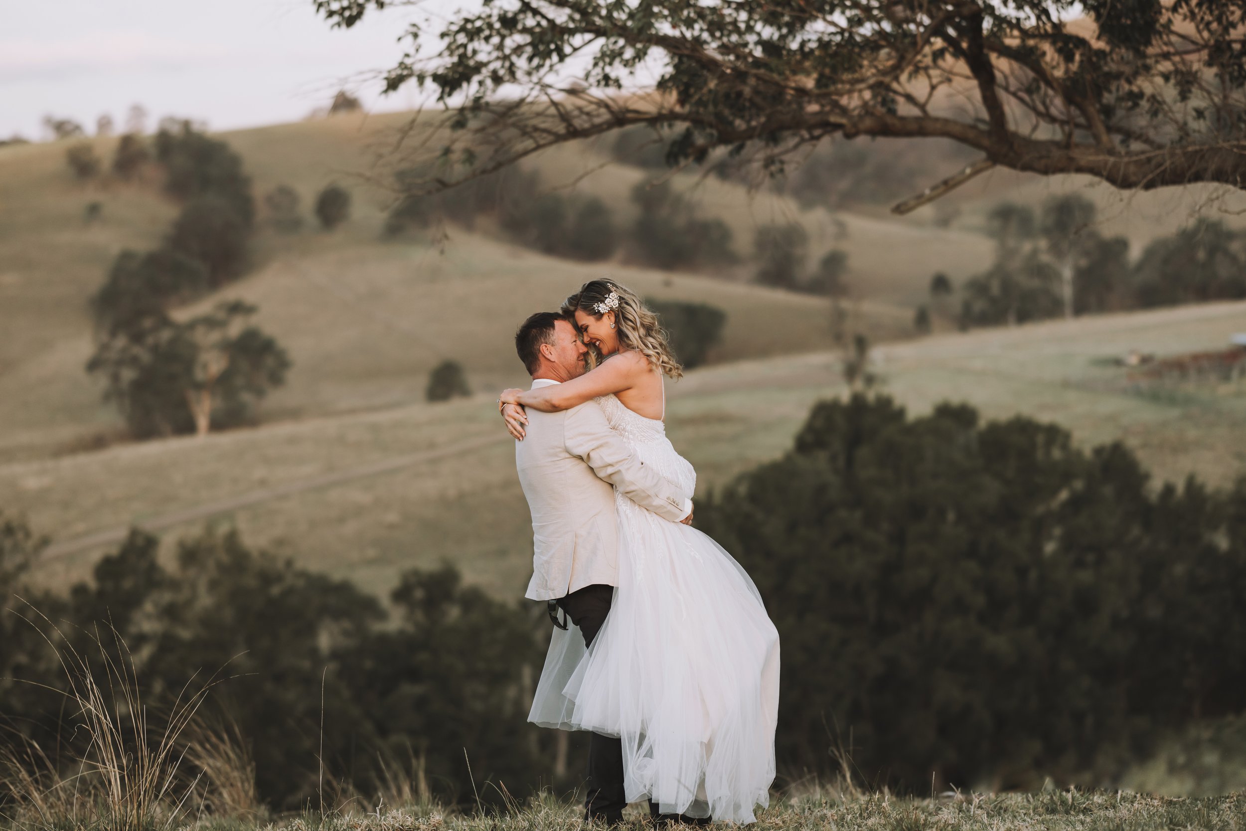 Bride being lifted in countryside – Elley and Lloyd wedding by Nicole Butler Photography