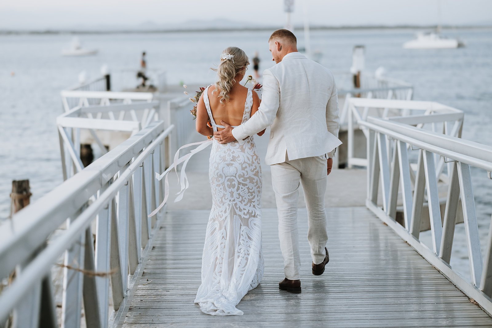 Newlyweds strolling along the picturesque jetty at Shoal Bay, captured by Nicole Butler Photography.