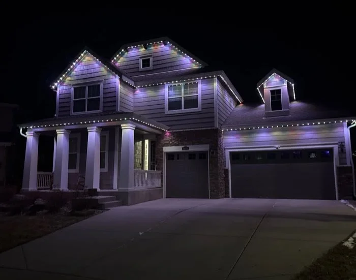 Two-story home with pastel permanent roofline lighting over the porch and garage