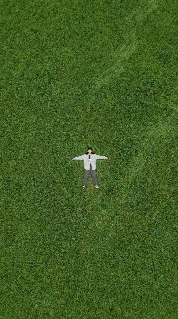 A person lying arms out in tall grass, seen from above