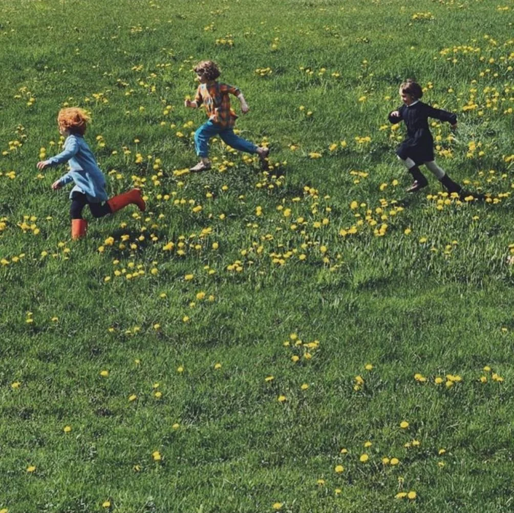 Three kids running across a grassy field full of dandelions