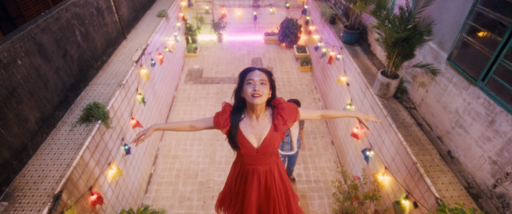 Mộng Hoài in a red dress, arms open on a lantern-lit path