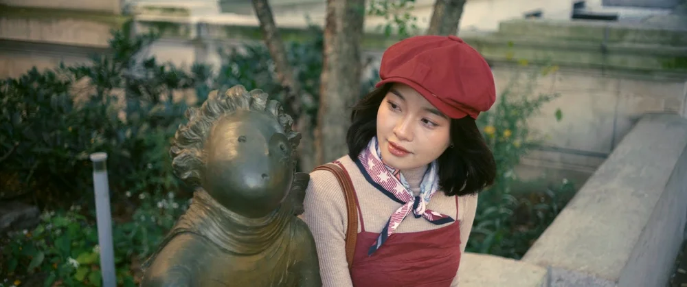 Mộng Hoài in a red beret beside a bronze statue
