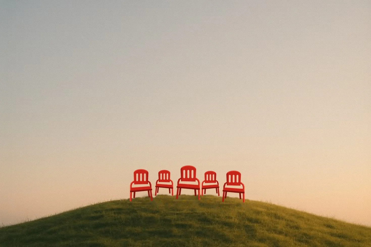 Red plastic chairs set out on a grassy hilltop at golden hour