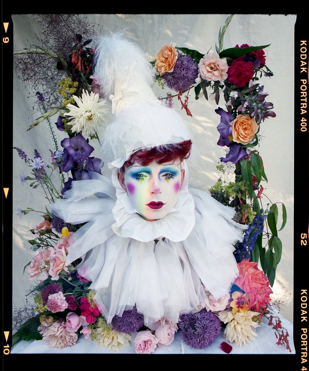 Editorial drag portrait: Finn Love in a white ruff crowned with pastel flowers.