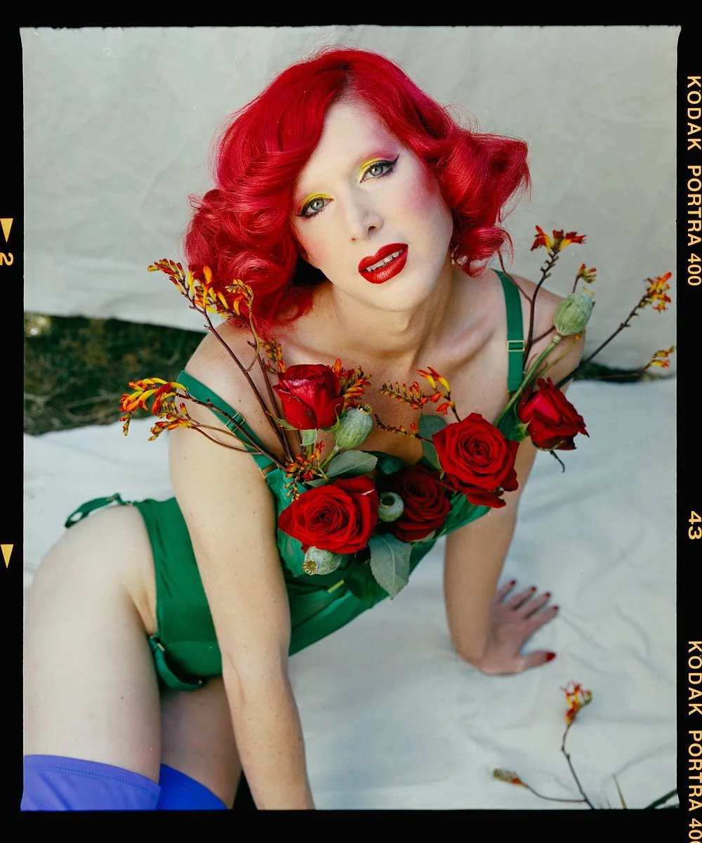 Drag portrait: Love Bailey reclining with red roses and red curls.