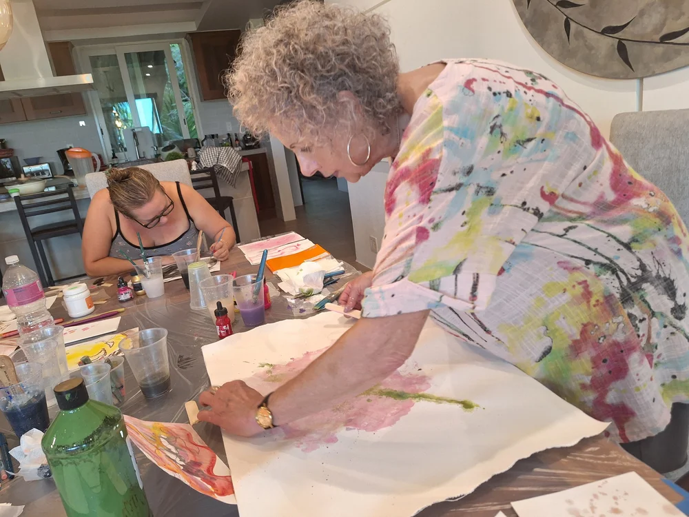 A guest bent over a large watercolour on a table full of paints