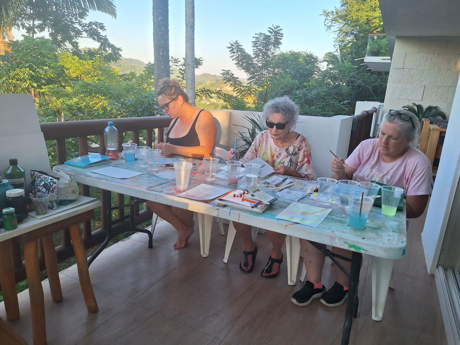 Three guests painting on a jungle balcony at golden hour