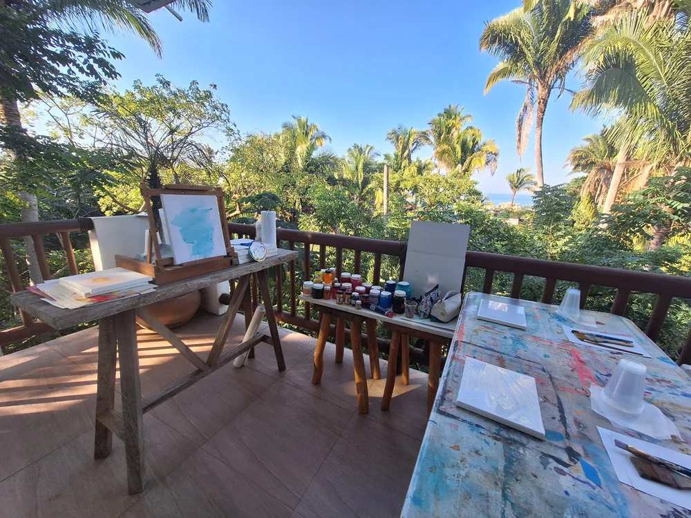 Painting tables set up on a balcony overlooking palms and the ocean