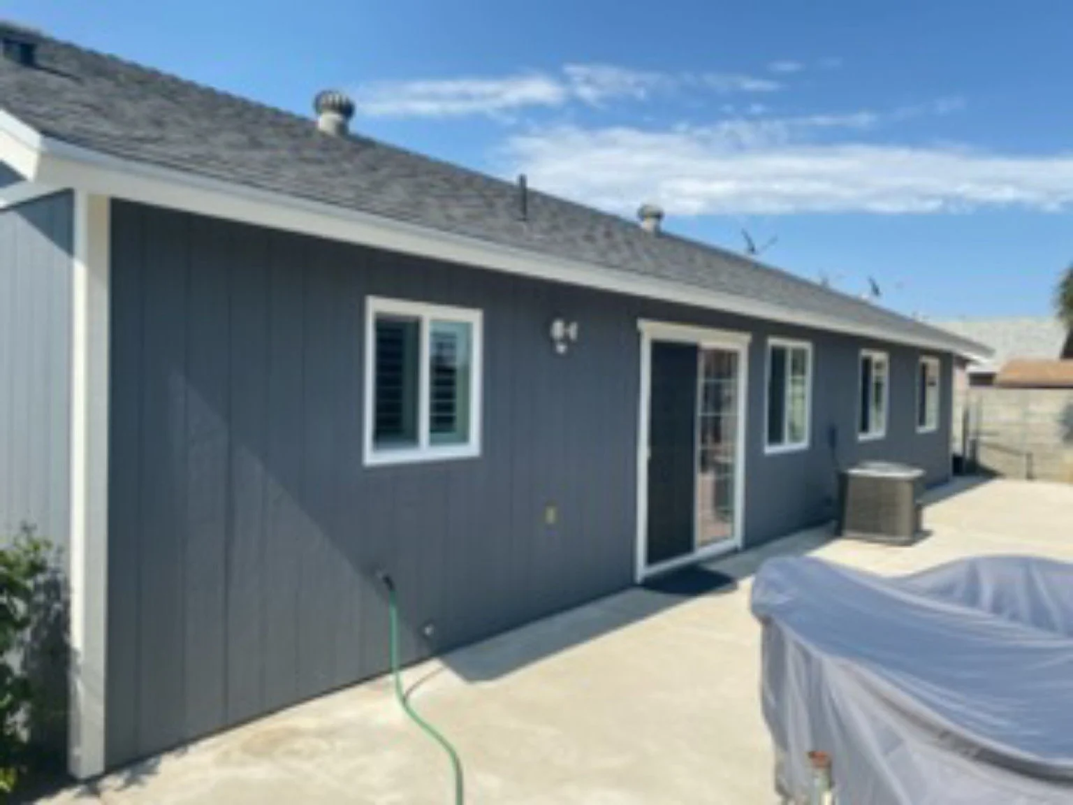 Gray-sided home exterior with white-trimmed windows and patio door