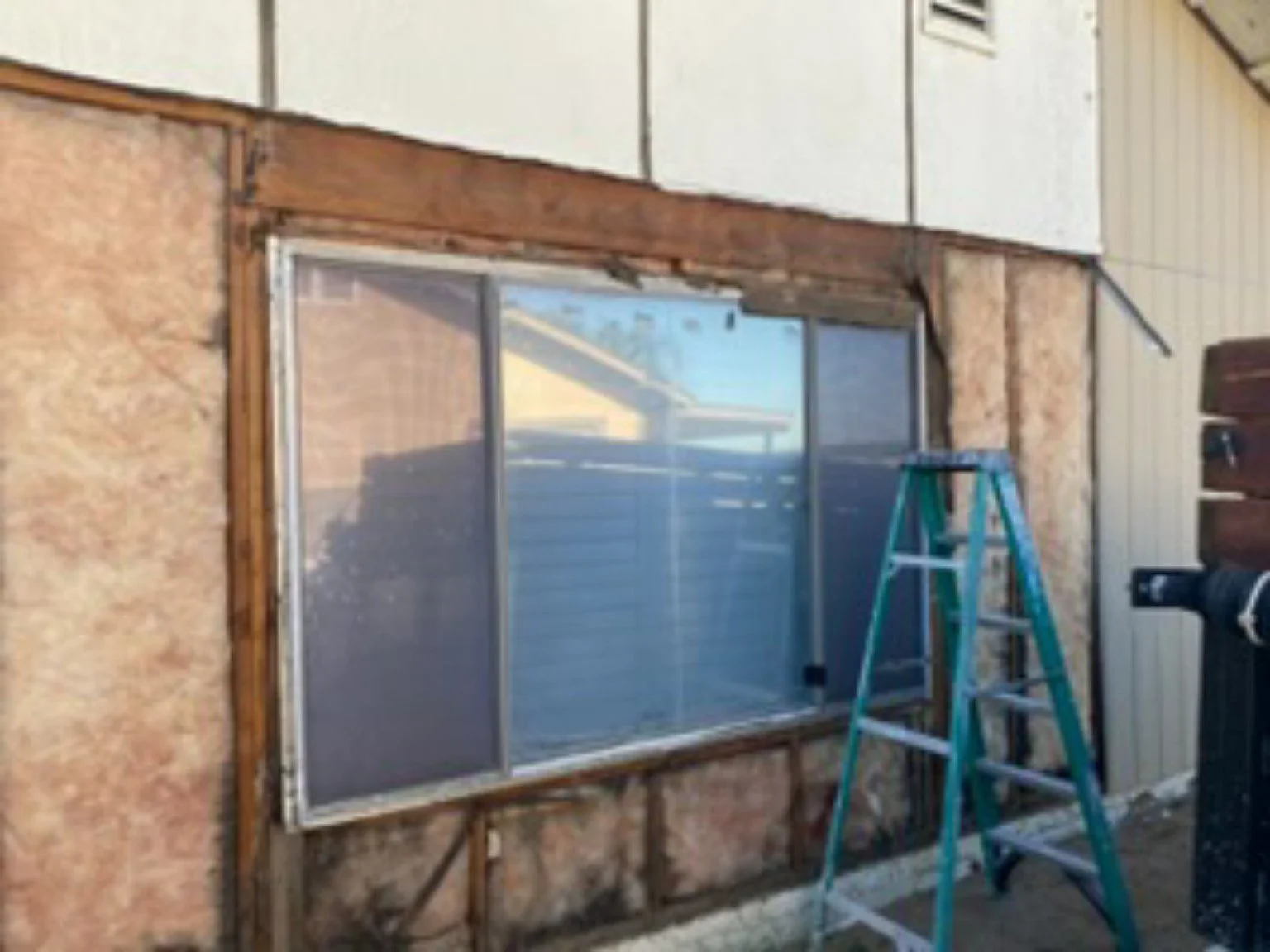 Window in an exposed wall opening with a ladder beside it.