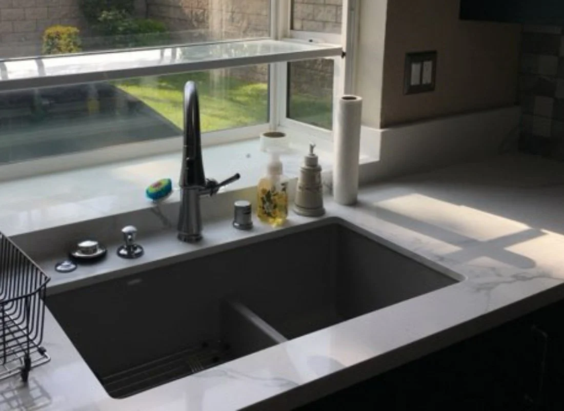 Kitchen sink and faucet beneath a projecting window.