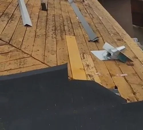 Exposed timber roof decking with loose metal pieces and a dark underlayment edge