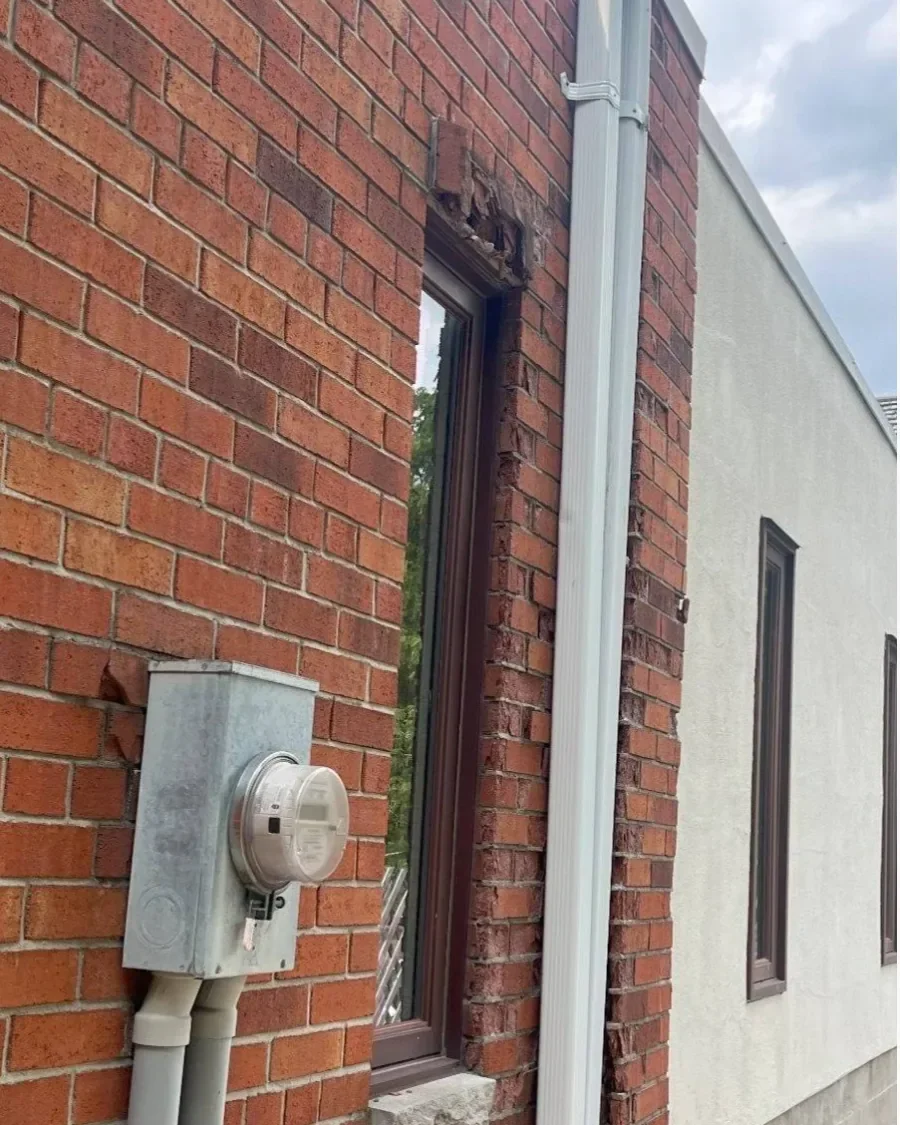Brick deterioration around exterior opening with adjacent downspout context.