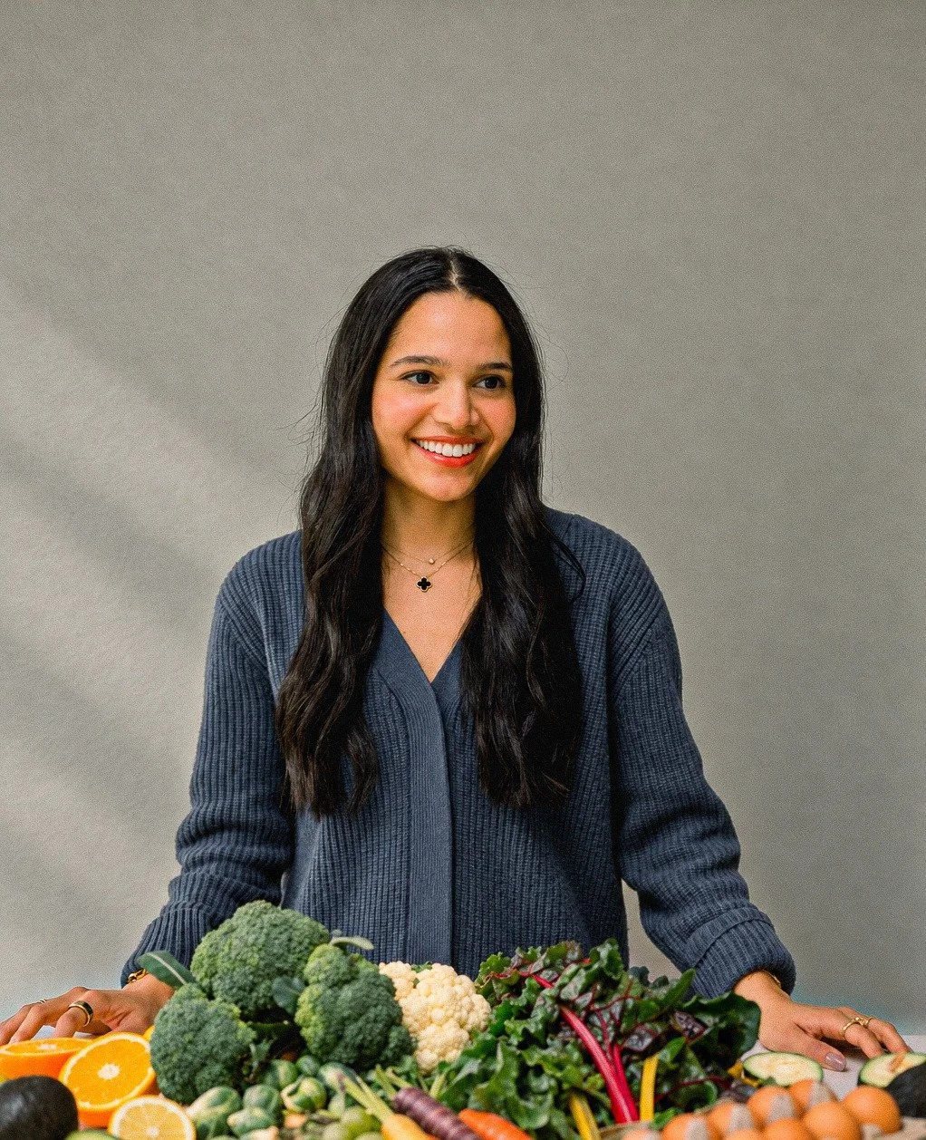 Ziba Klein, Functional Nutritionist, smiling behind a table of fresh produce