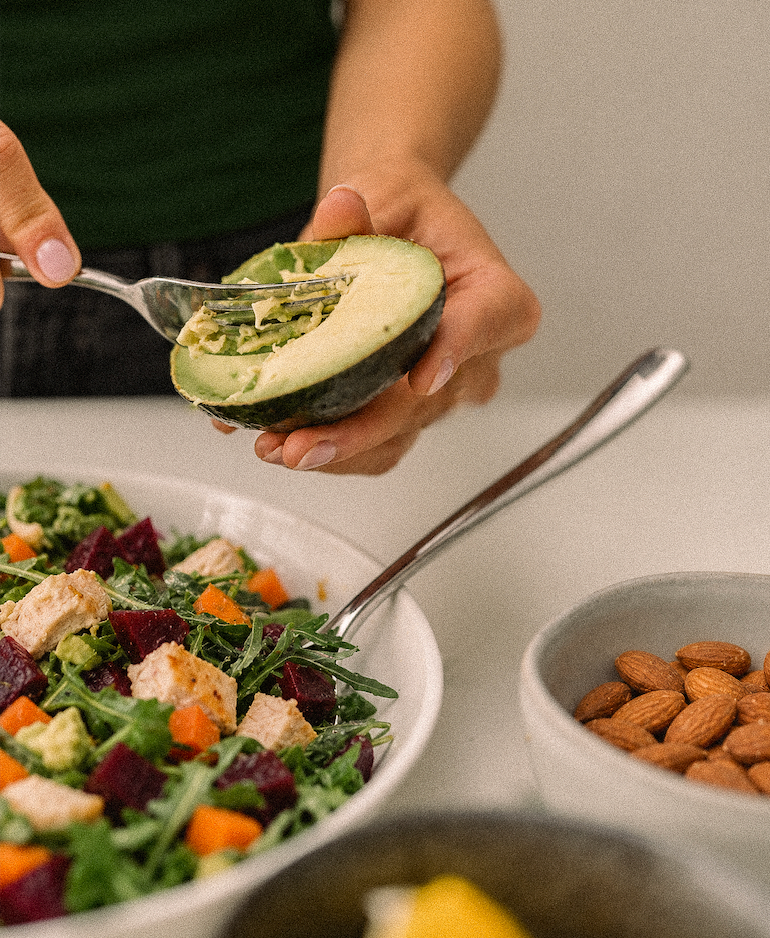Preparing avocado alongside a colorful salad and almonds