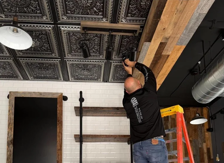 Ohm Solutions Group technician aiming track lighting beneath a pressed-metal ceiling