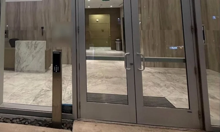 Glass lobby entry at night with a pedestal-mounted video intercom beside the doors