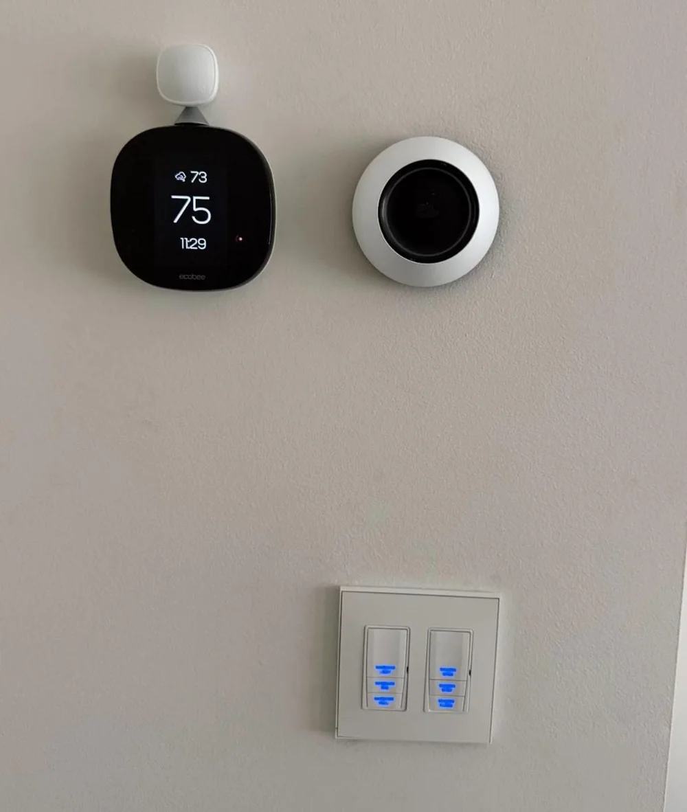 Smart thermostat and room sensor above a backlit lighting keypad on a painted wall