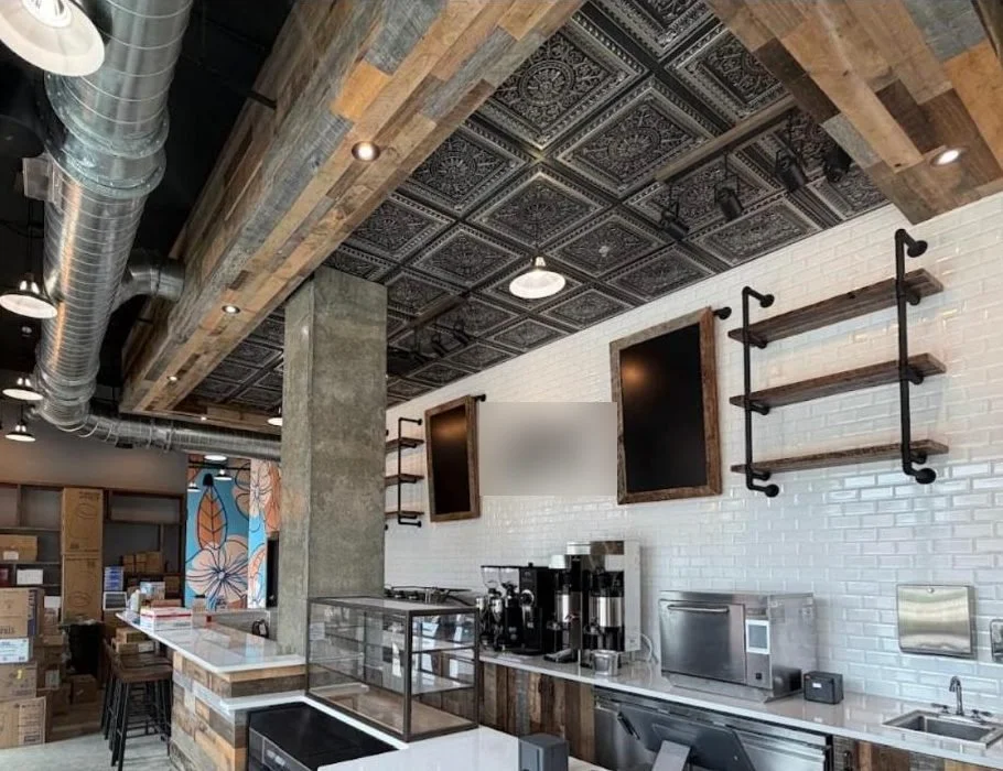 Café interior with pressed-metal ceiling, reclaimed wood beams, track lighting and service counter