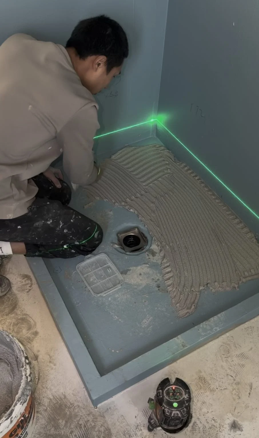 Adhesive being notched on the shower floor with a green laser line across it, Greenhithe family bathroom