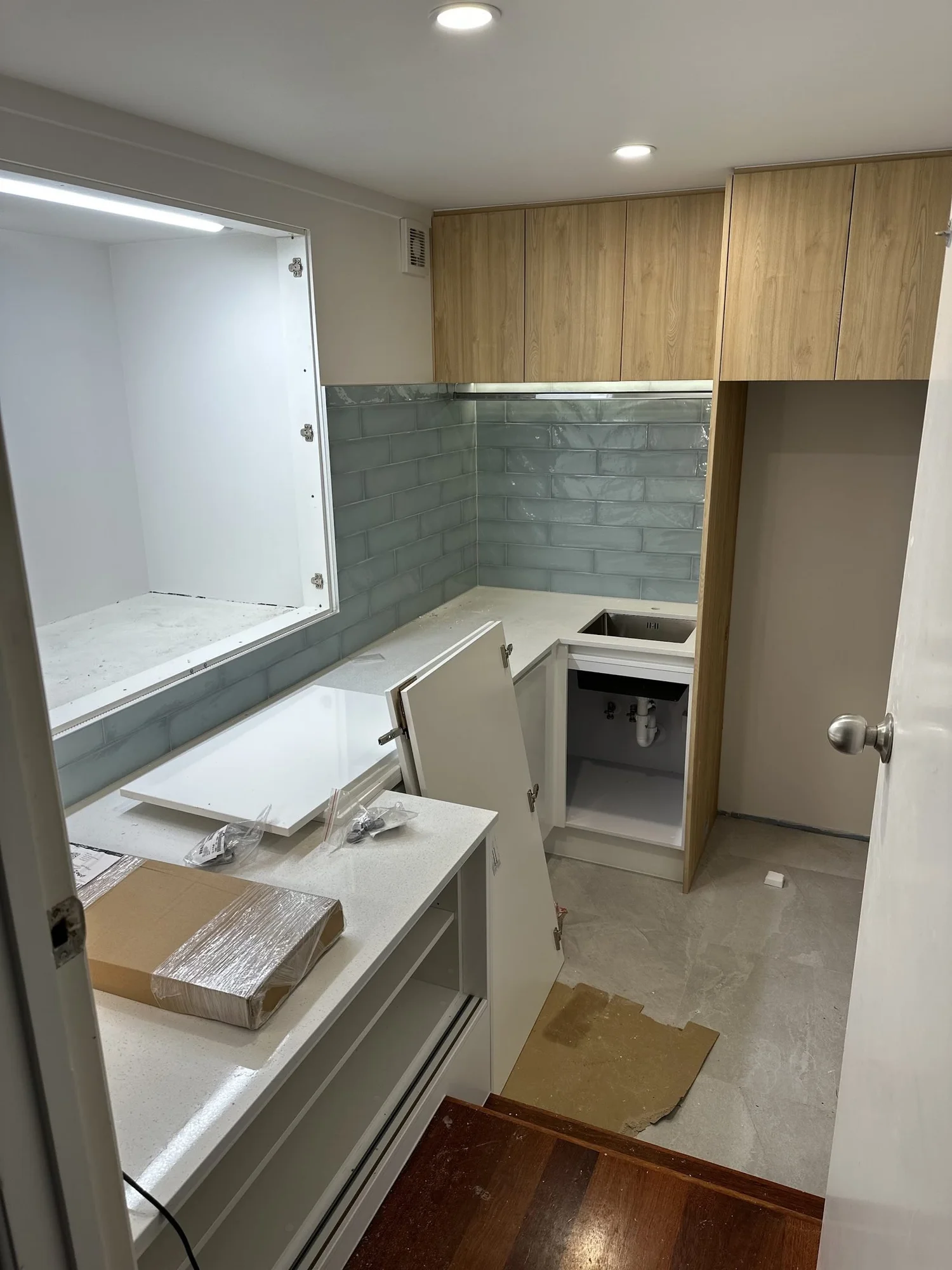 Fit-off stage of the St Heliers laundry showing sage tile, oak overheads and the lit recess