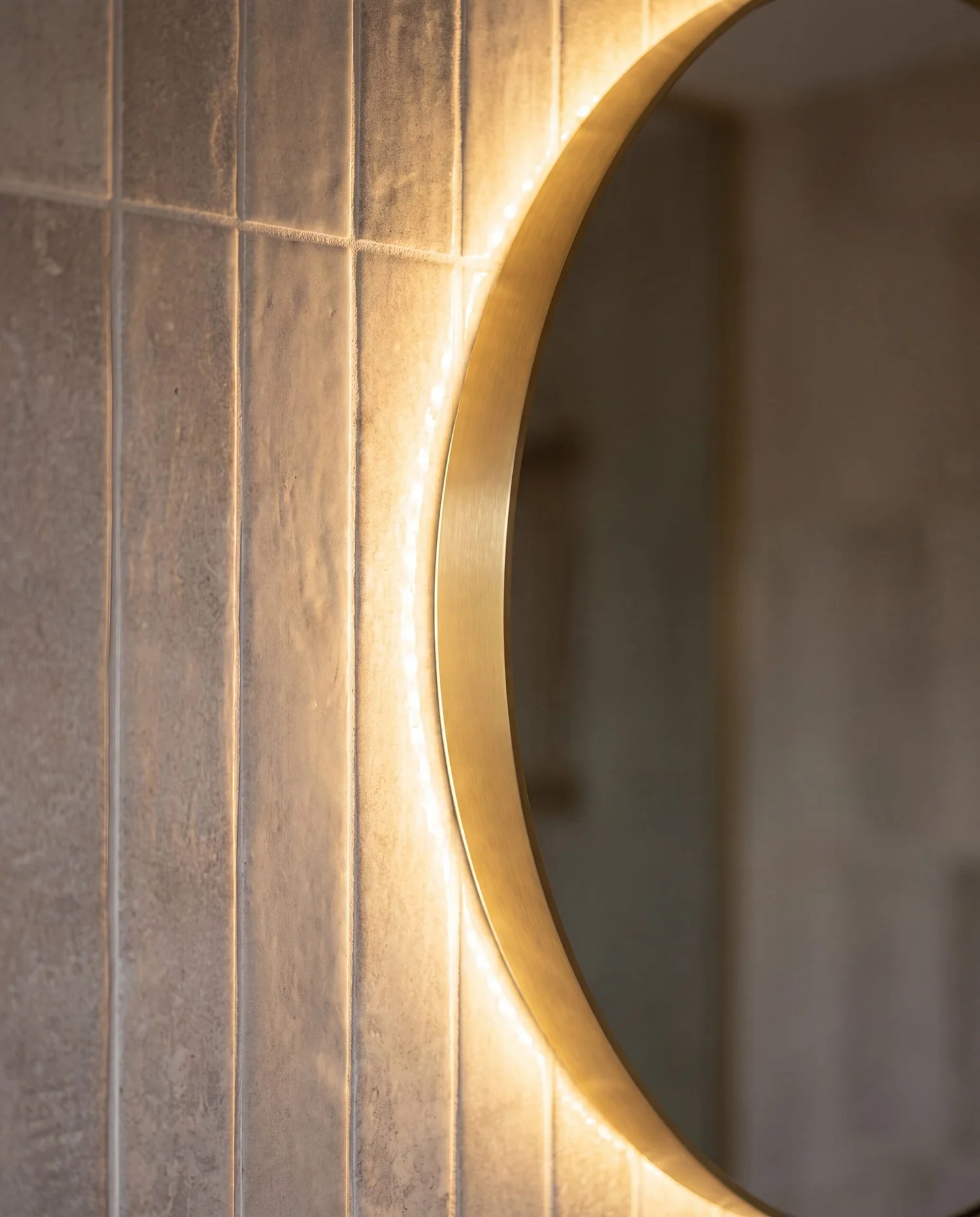 Backlit round brass mirror edge against grey vertical stack-bond tile, Garfield Street Parnell