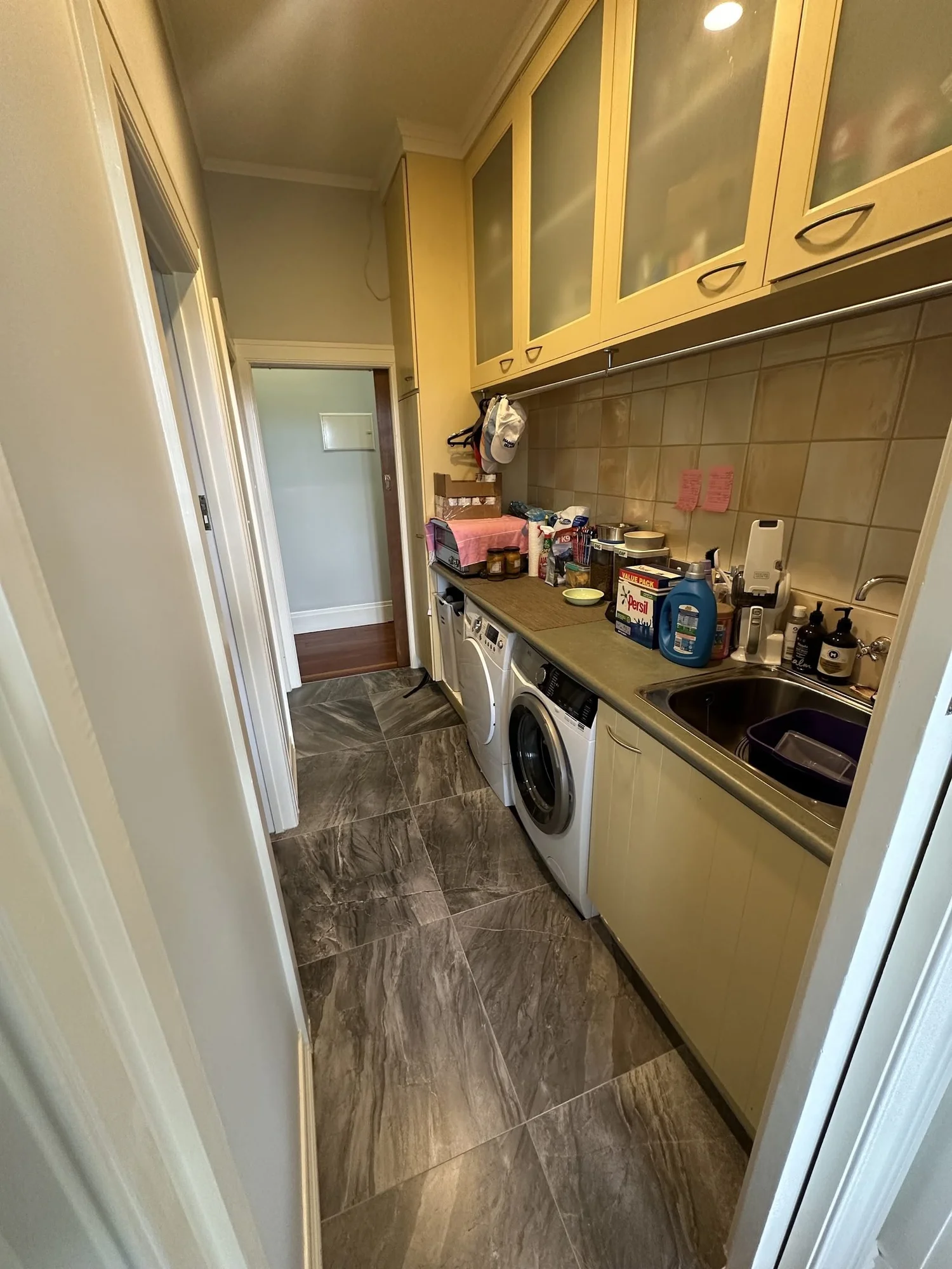 Dated 1990s galley laundry in Bayswater before renovation, cream melamine cupboards and beige tiles