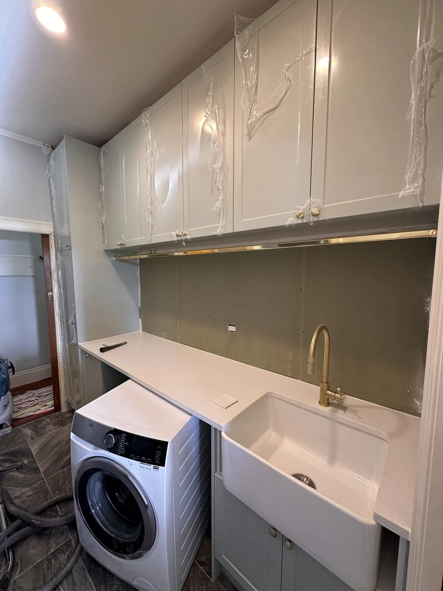 White fireclay butler sink and brushed brass tap installed against bare wet-area board