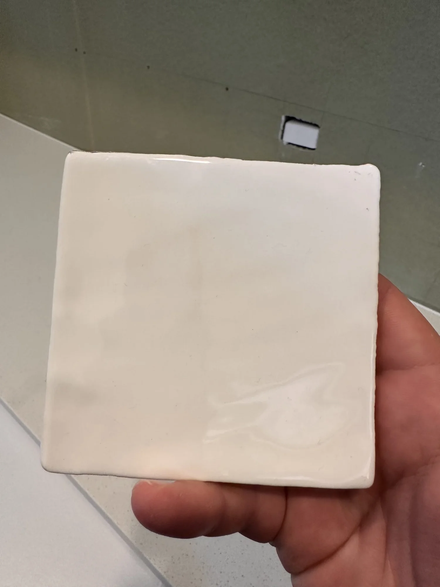 Handmade Zellige splashback tile sample held against the laundry wall