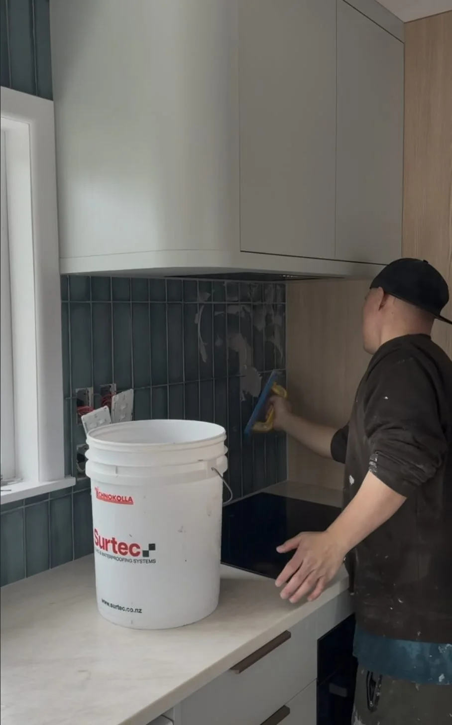 Tiler applying adhesive and setting the dark green vertical stack-bond splashback in the Belmont kitchen