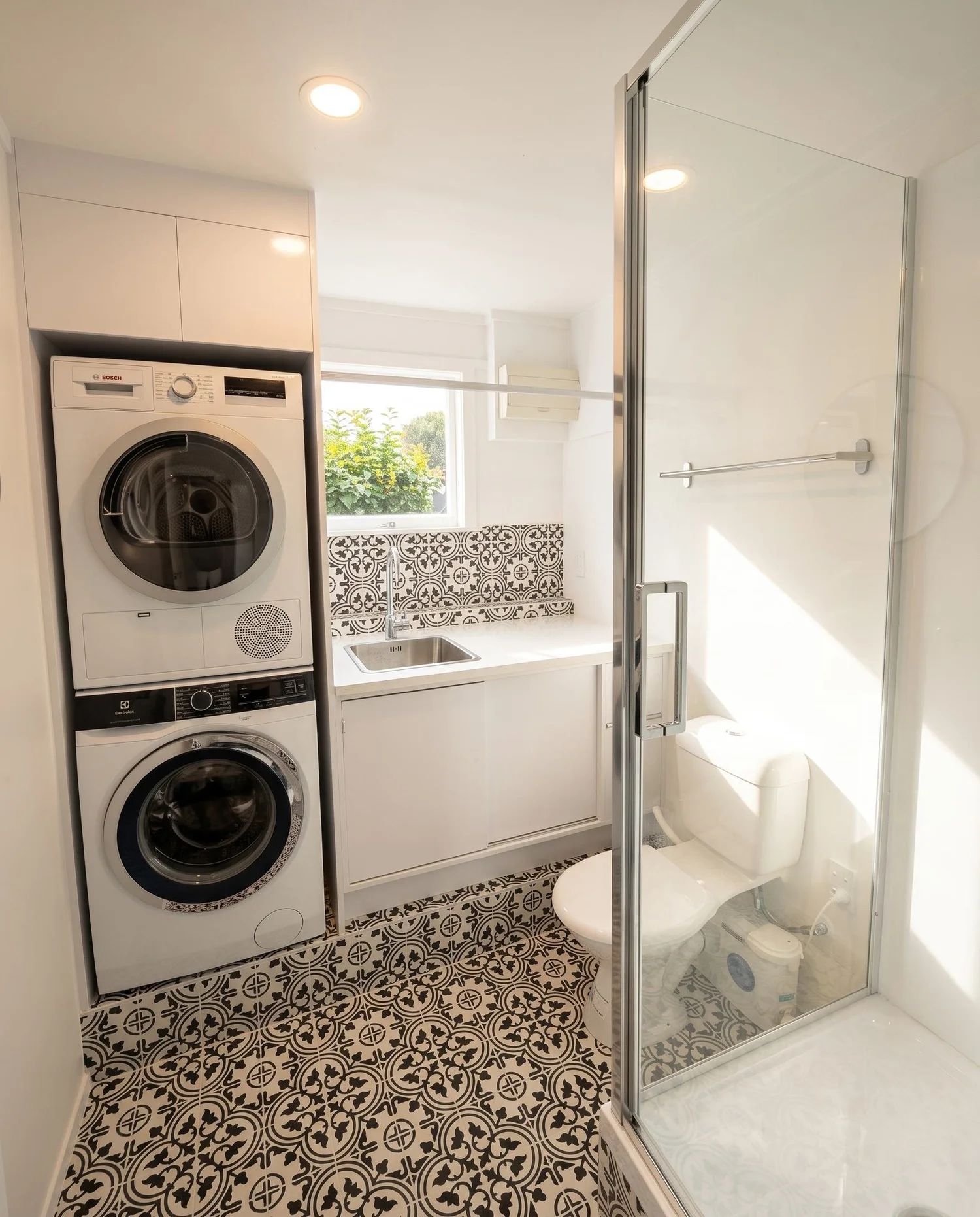 Finished Belmont laundry bathroom with frameless glass shower, stacked machines and encaustic tile floor