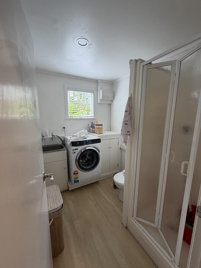 Merani Street laundry in Belmont before renovation, washer on the floor beside white cabinetry