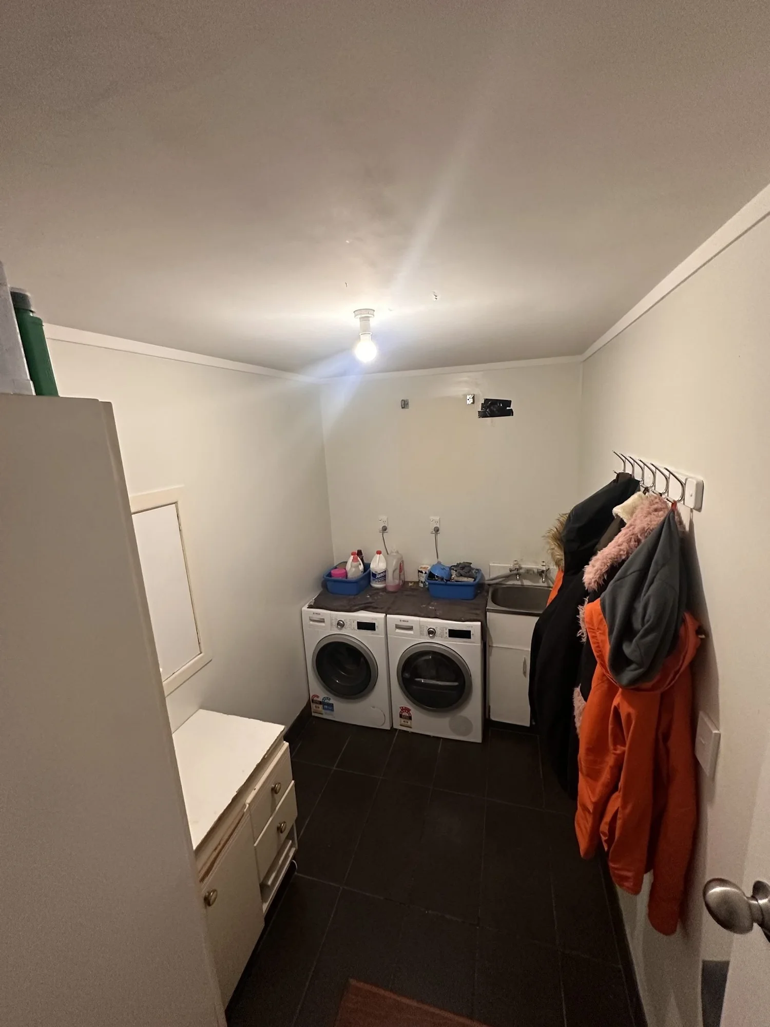 Rarangi Road laundry in St Heliers before renovation, charcoal floor tile and cluttered cream cabinetry
