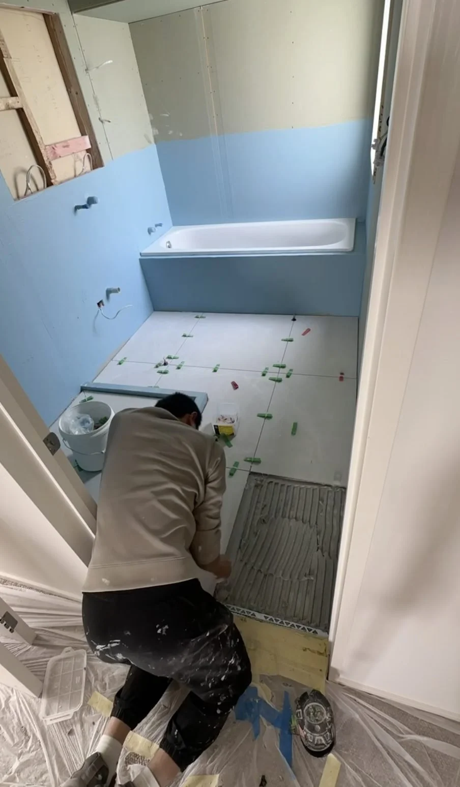 Large-format floor tile being laid beside the bath with levelling clips, Churchouse Road Greenhithe