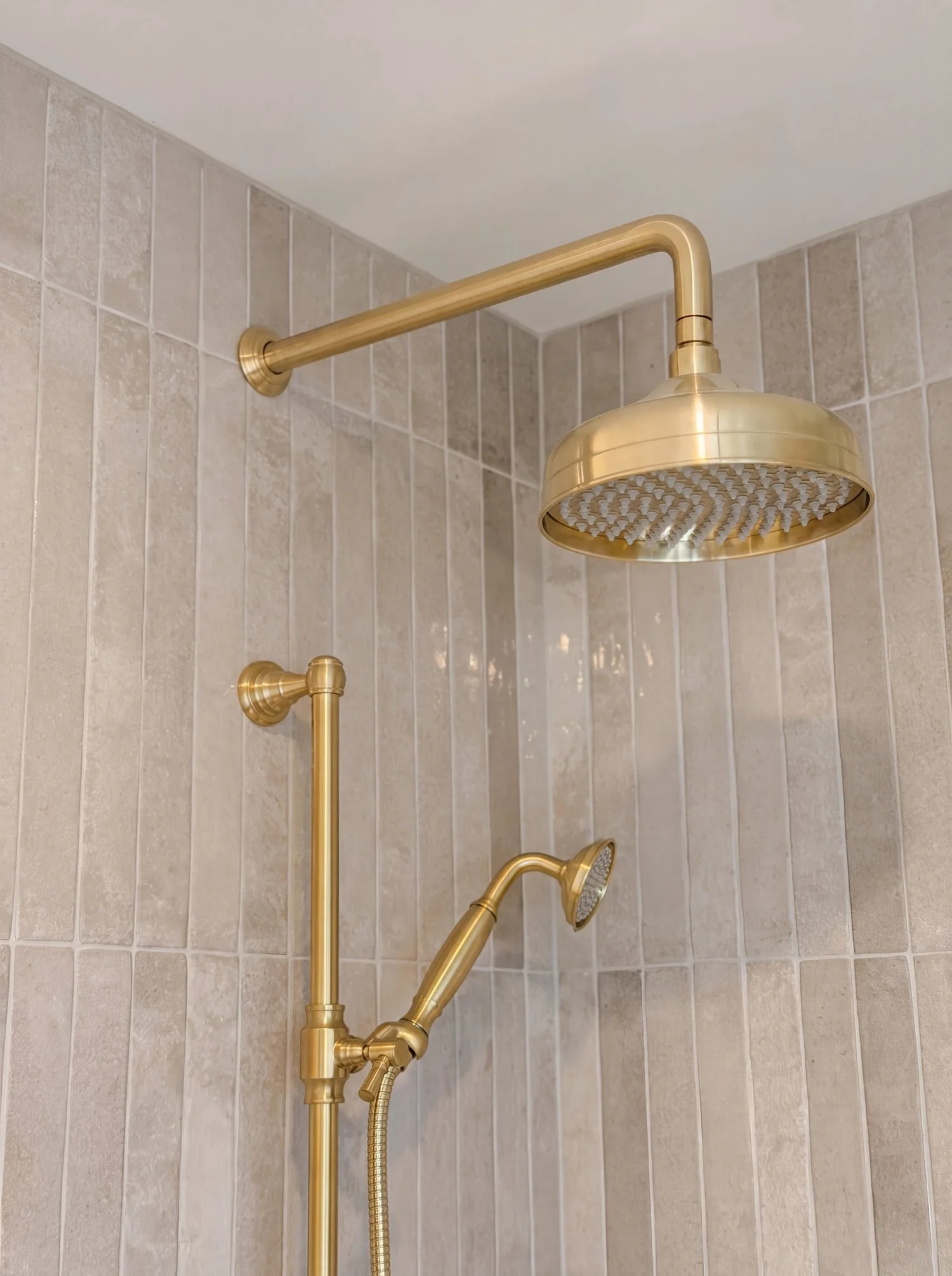 Brushed brass rain shower head and handheld on rail against grey vertical stack-bond tile, Parnell