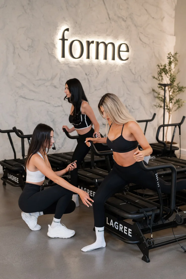 A Forme instructor coaching a client on the Lagree machine in front of the forme wall