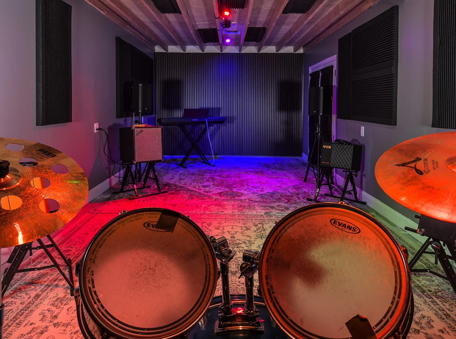 View from the drum kit across The Jam Space, with amplifiers, a keyboard, and colorful room lighting