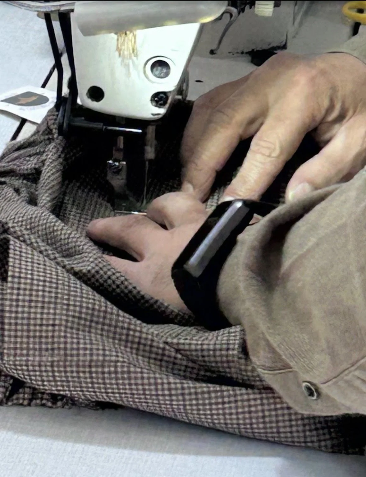 Hands sewing a checked womenswear garment at Pure Design Fashion’s sample atelier in Turkey.