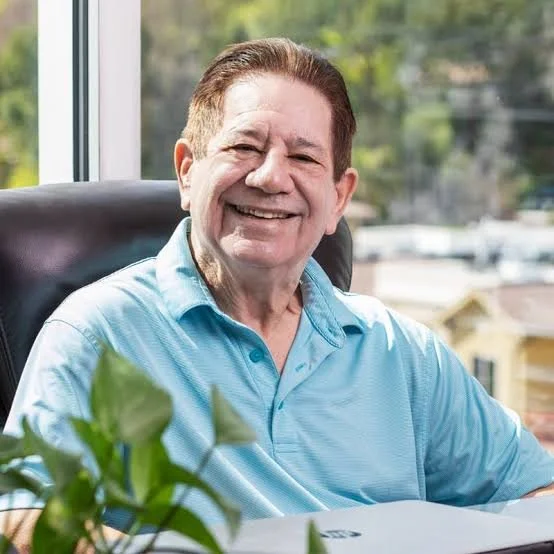 Dr. Robert Jaffe seated at his desk in his Encino office, smiling, with natural light from the window behind him