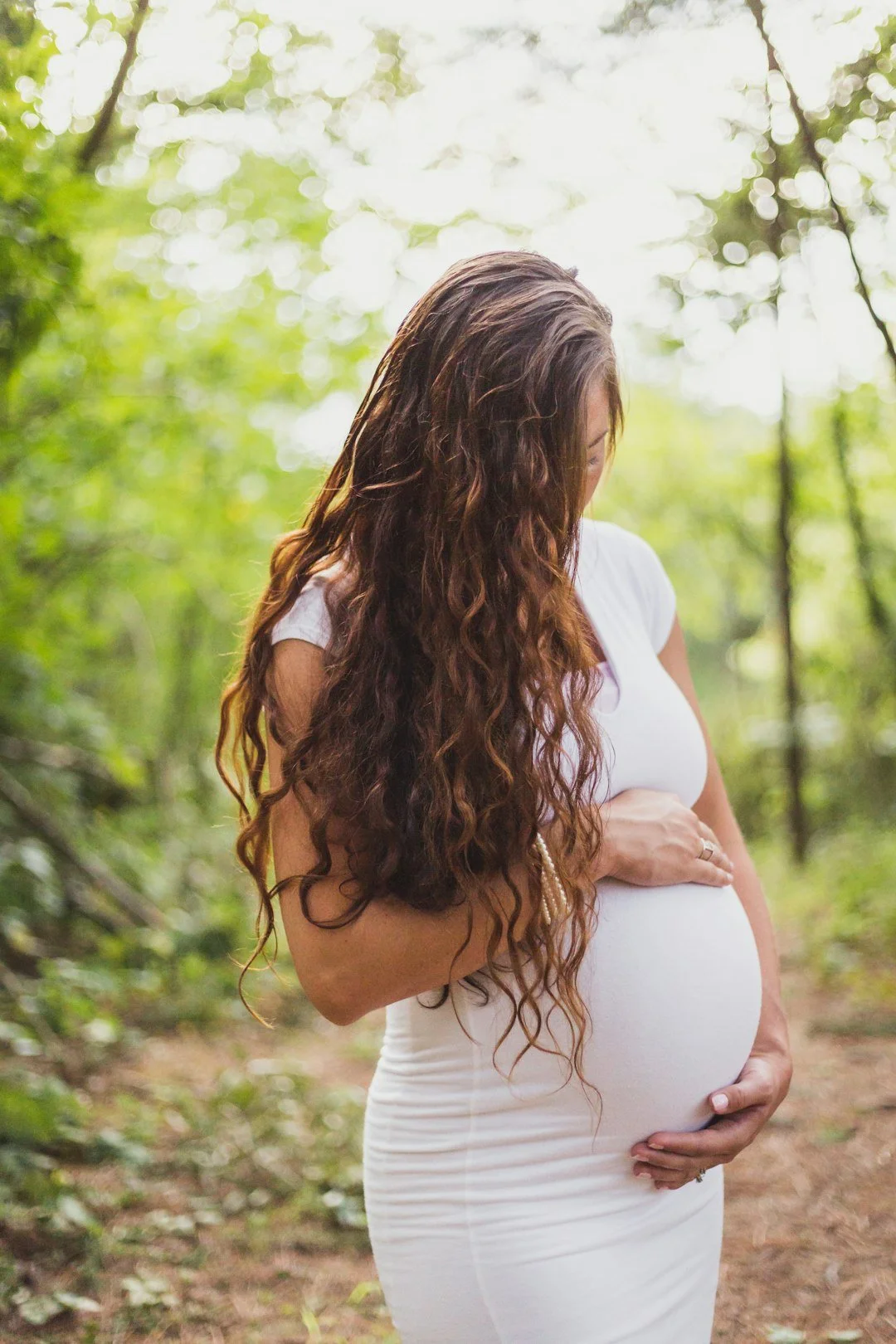 Pregnant mother holding her back with gentle smile outdoors