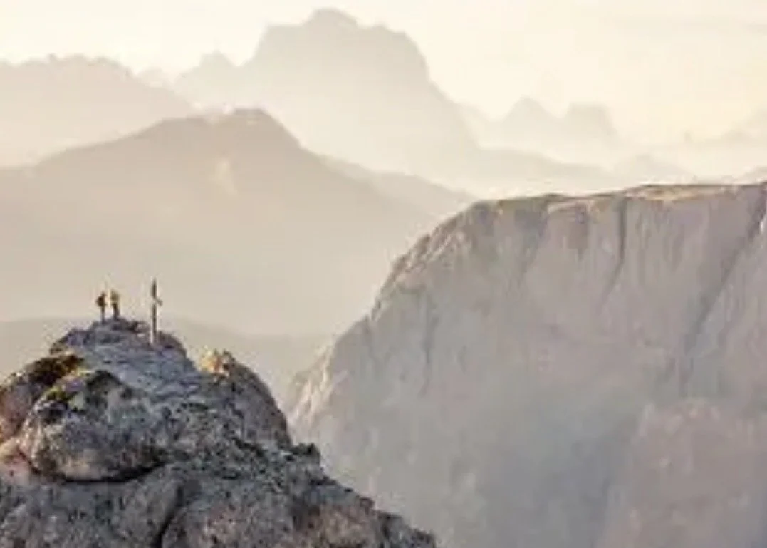 Hikers at a summit cross in the Dolomites at dawn